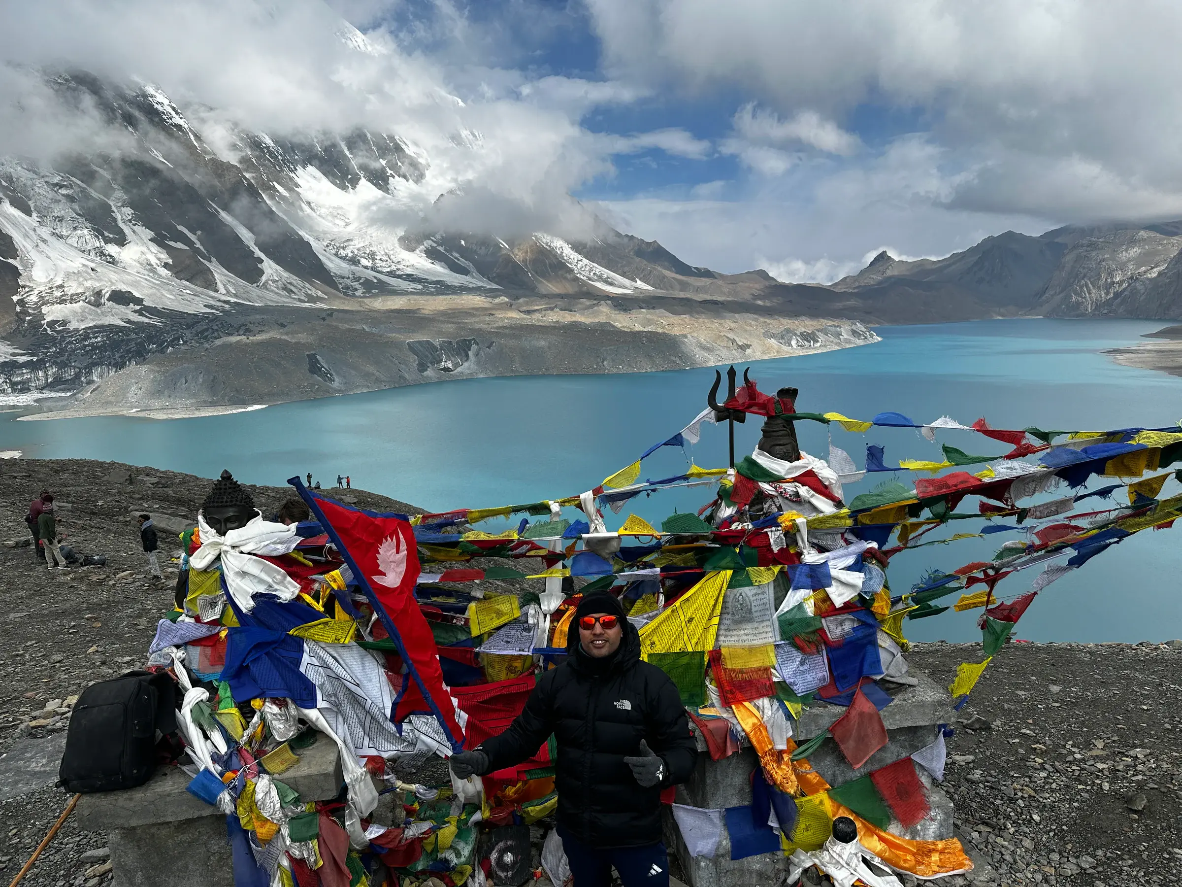 Khagendra beside a turquoise Himalayan lake with Nepal's flag and snow-covered peaks