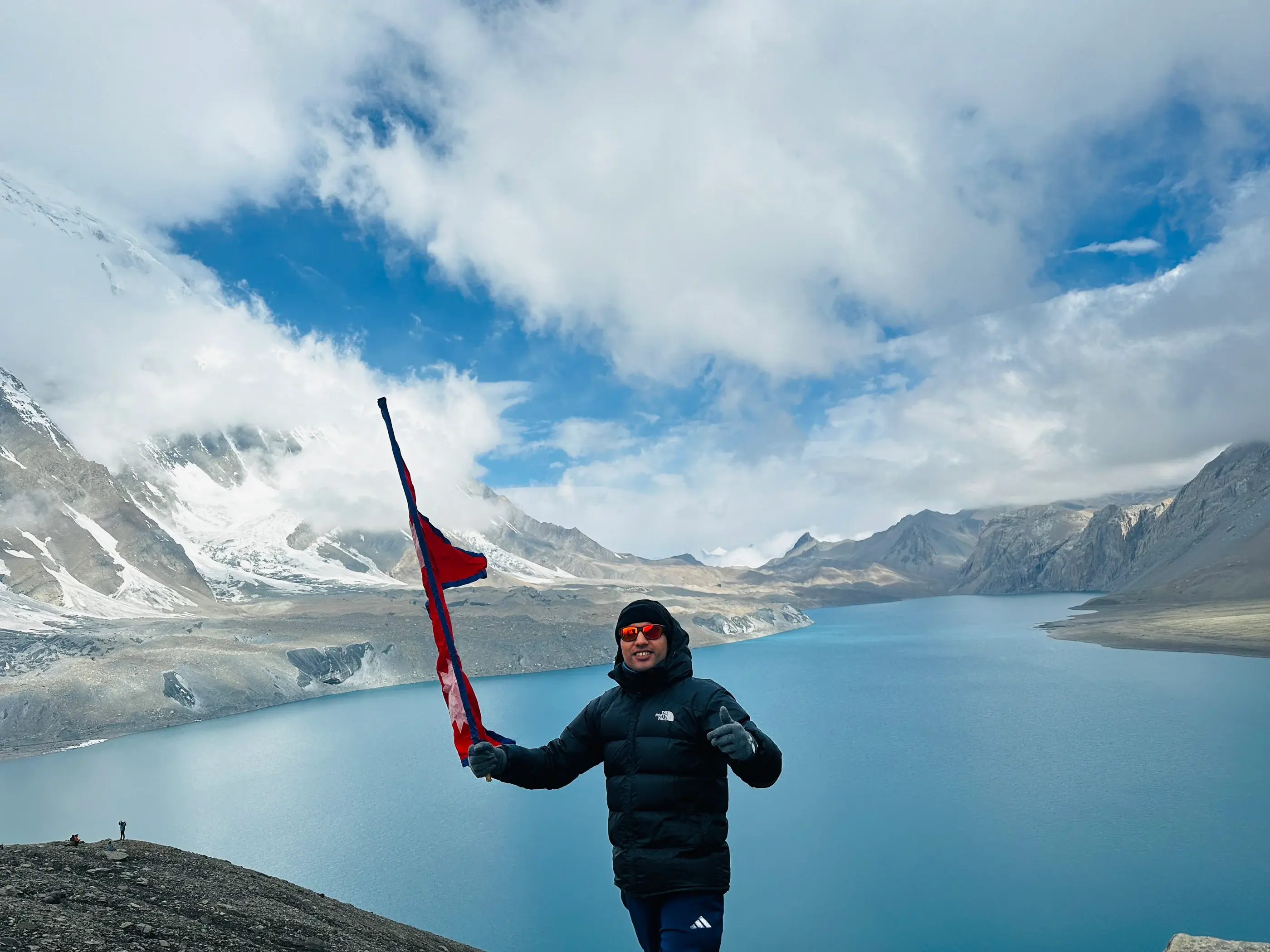 Khagendra holding Nepal's flag above the turquoise water of Tilicho Lake